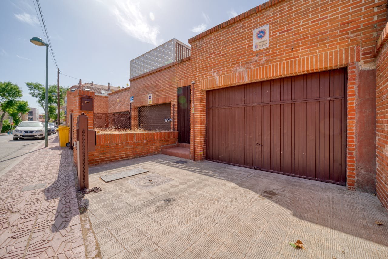 Sunny day outside a red brick house with garage in a quiet neighborhood.