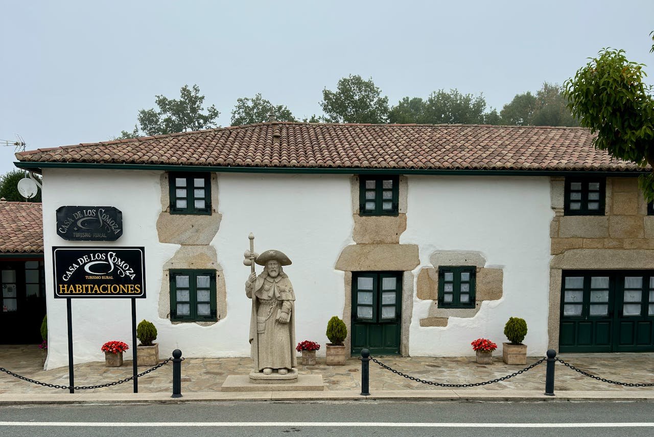 Cozy rural house with stone facade and historic statue in a quaint setting.