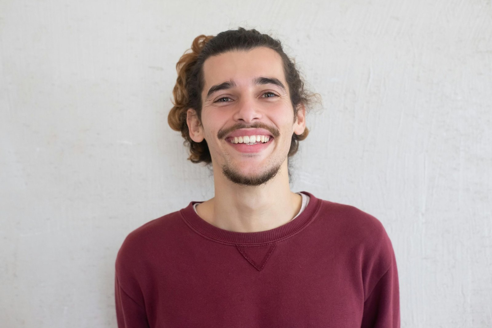 Portrait of a smiling man with facial hair and curly hair wearing a red sweater.